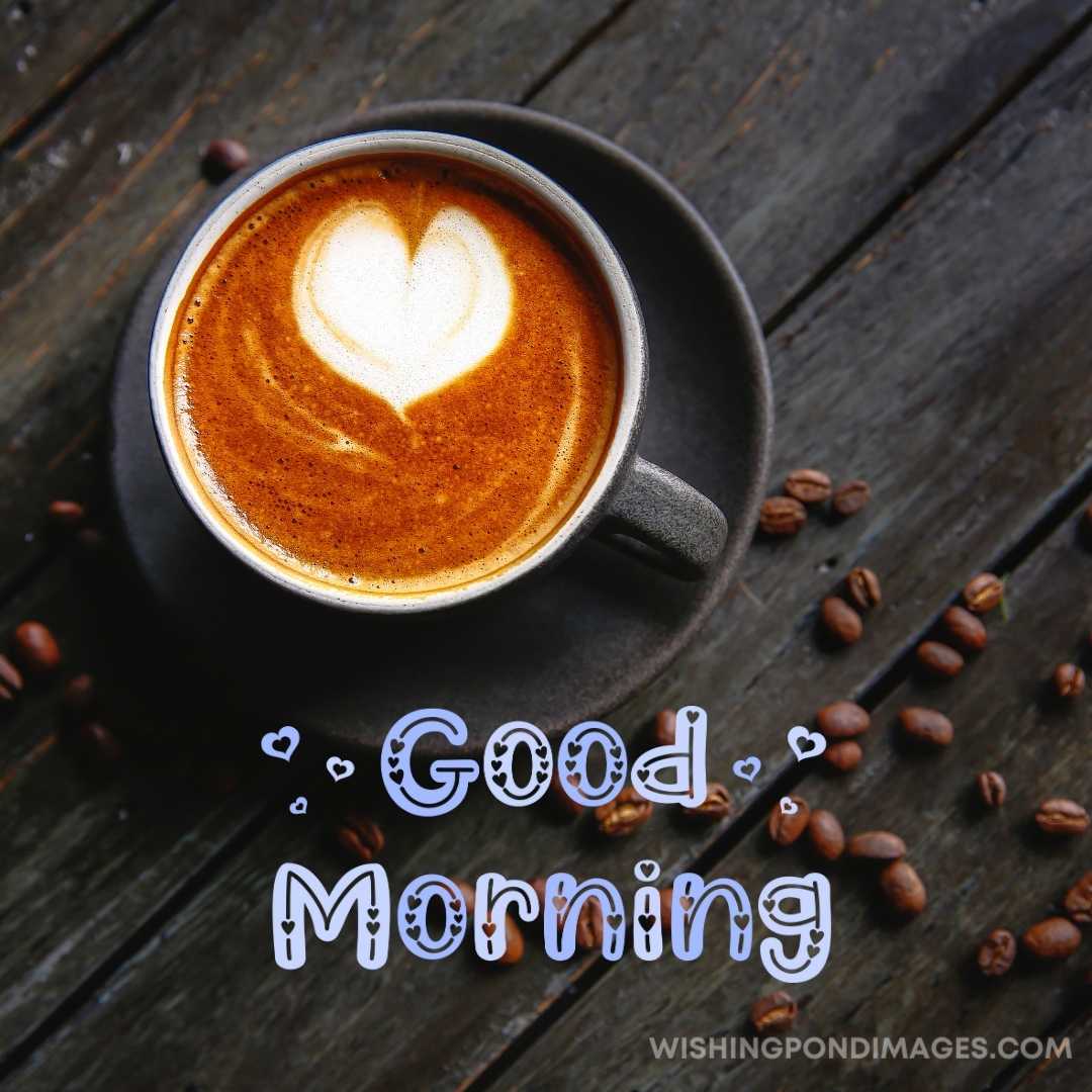 A cup of coffee in a black-colored cup and plate on the table with coffee beans. Good Morning Coffee